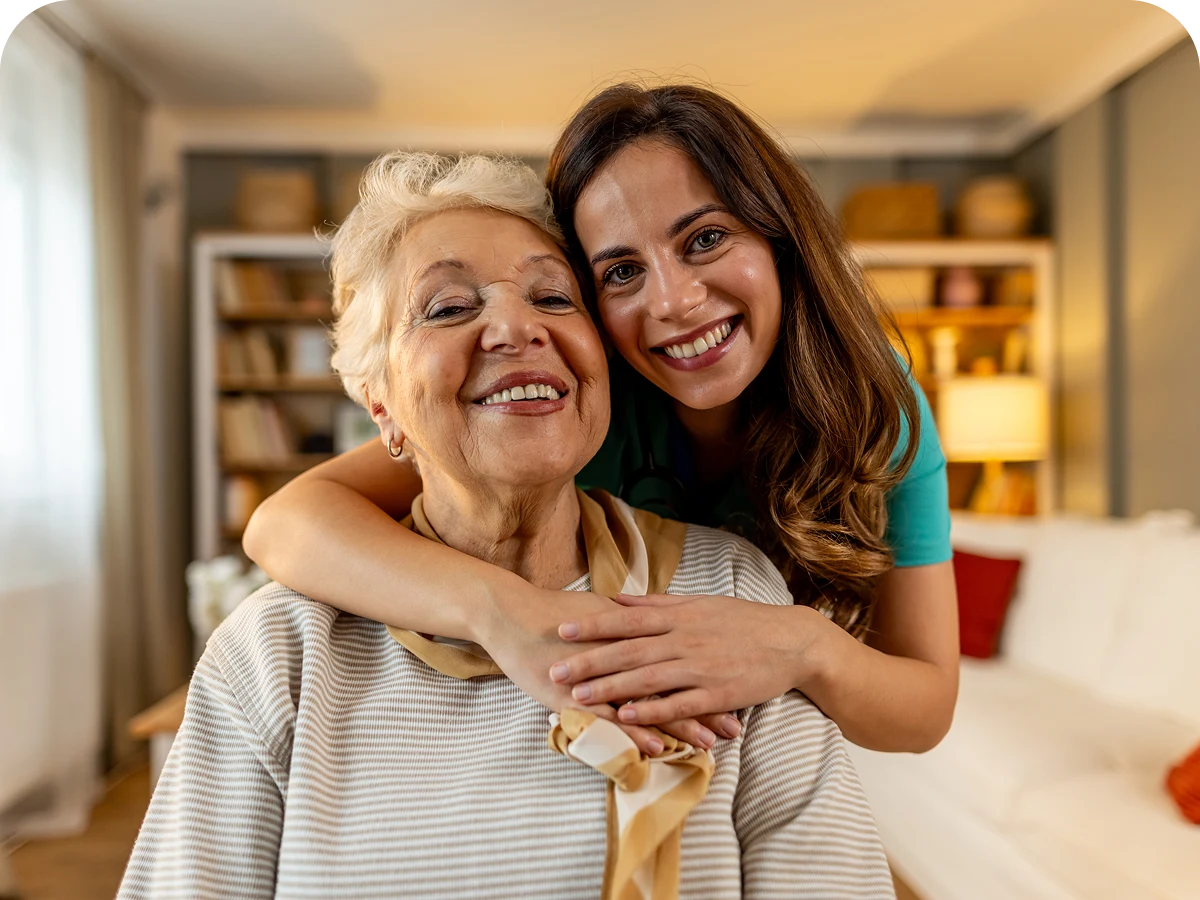 Smiling woman hugging elderly woman indoors.