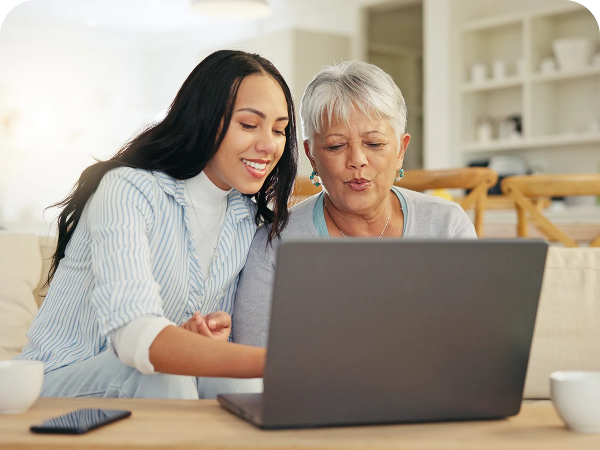 Two women using a laptop together, smiling.
