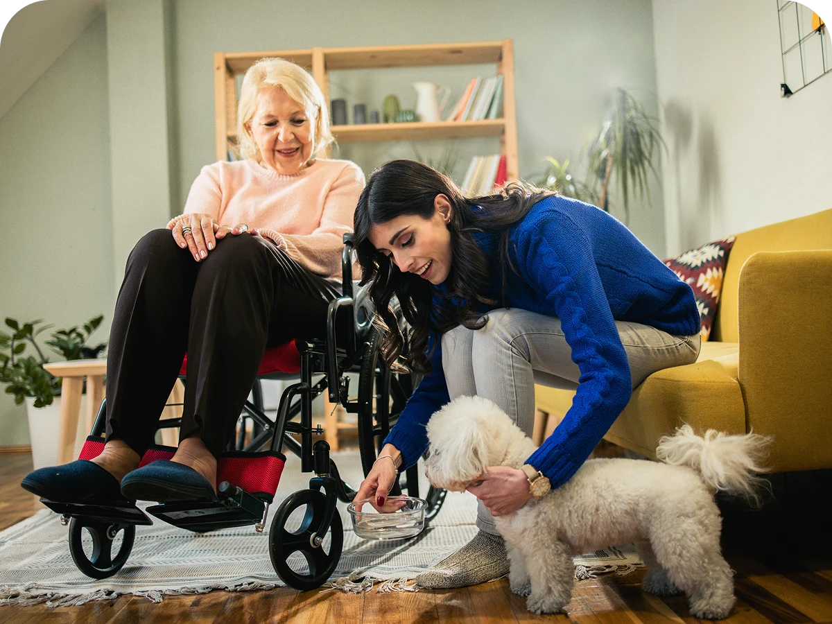 Woman feeding dog beside elderly lady in wheelchair.